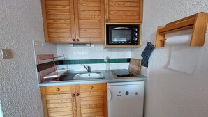 Una cocina compacta con armarios de madera, microondas, fregadero y lavavajillas.