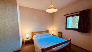 Habitación individual con una cama y cabecera de madera, dos lámparas de noche, una ventana con cortinas y pared con textura.
