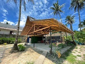 A tropical resort with a thatched-roof structure, palm trees, and a clear blue sky. - Dawn Patrol Hostel (General Luna)