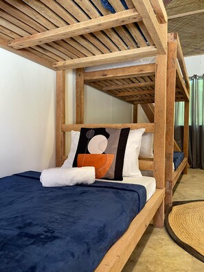 A wooden bunk bed with a blue mattress and a pillow with an abstract design. - Dawn Patrol Hostel (General Luna)