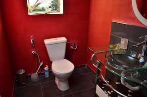 A bathroom with a red wall, a white toilet, a glass sink, and a small trash bin. - Room-the Romantic Atmosphere of the red (Antananarivo)