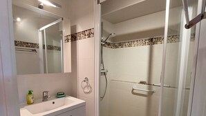 A bathroom with a white sink, a mirror, a towel ring, and a shower area with a glass door. - Charming apartment in Méaudre - 5 pers, parking included (Méaudre)