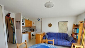 A compact living space with a kitchenette, a dining area with a blue polka dot table, a sofa, and a bookshelf. - Charming apartment in Méaudre - 5 pers, parking included (Méaudre)