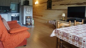 A cozy living room with a sofa, a television, and a dining table with a tablecloth. - Renovated apartment with balcony, parking and wifi, close to slopes - Méaudre (Méaudre)