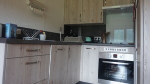 A kitchen with wooden cabinets, a built-in oven, and a countertop with various kitchen items. - Renovated apartment with balcony, parking and wifi, close to slopes - Méaudre (Méaudre)