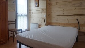 A bedroom with a wooden wall, a bed, a chair, and a window with curtains. - Renovated apartment with balcony, parking and wifi, close to slopes - Méaudre (Méaudre)