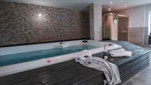 Een wellnessruimte met een ruime jacuzzi, houten vloeren en een stenen muur.