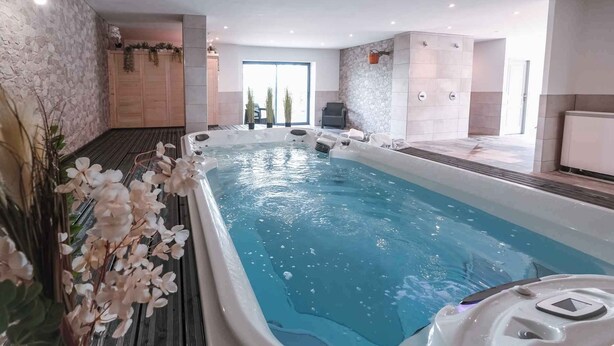Een modern binnenzwembad met een whirlpool, omgeven door stenen muren en een houten vloer.