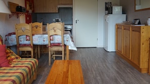 A cozy room with a bed, a wooden table, a kitchen area with cabinets and a microwave, and a door leading to another room. - Apartment in Méaudre - 4 pers, near center, balcony, parking (Méaudre)