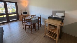 Un comedor con mesa y sillas, una pequeña cocina con tostadora, y vistas a través de grandes ventanales.