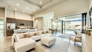 A spacious living room with a large sectional sofa, a kitchen with modern appliances, and a view of a pool area. - Villa Escape - brand new, with pool and spa, on water with gulf access (Cape Coral)