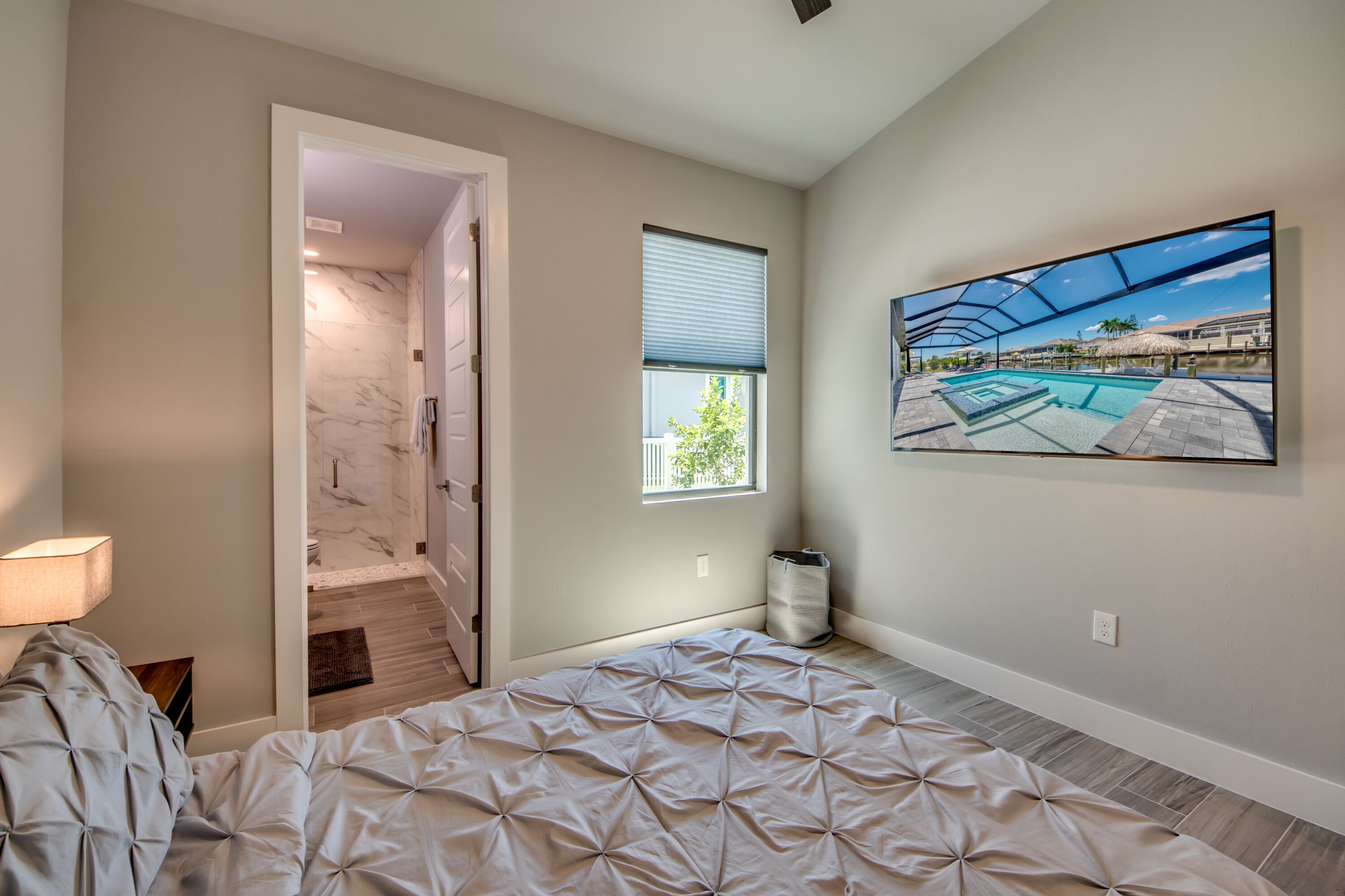 Quarto com cama, janela, pintura de uma piscina e corredor que leva a um banheiro.