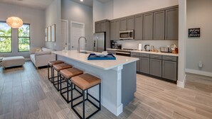 A modern kitchen with a large island, grey cabinets, and a bar stool seating area. - Villa Escape - brand new, with pool and spa, on water with gulf access (Cape Coral)