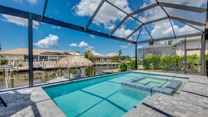A swimming pool with a clear blue water feature, surrounded by a covered patio area with a view of a tropical landscape. - Villa Escape - brand new, with pool and spa, on water with gulf access (Cape Coral)