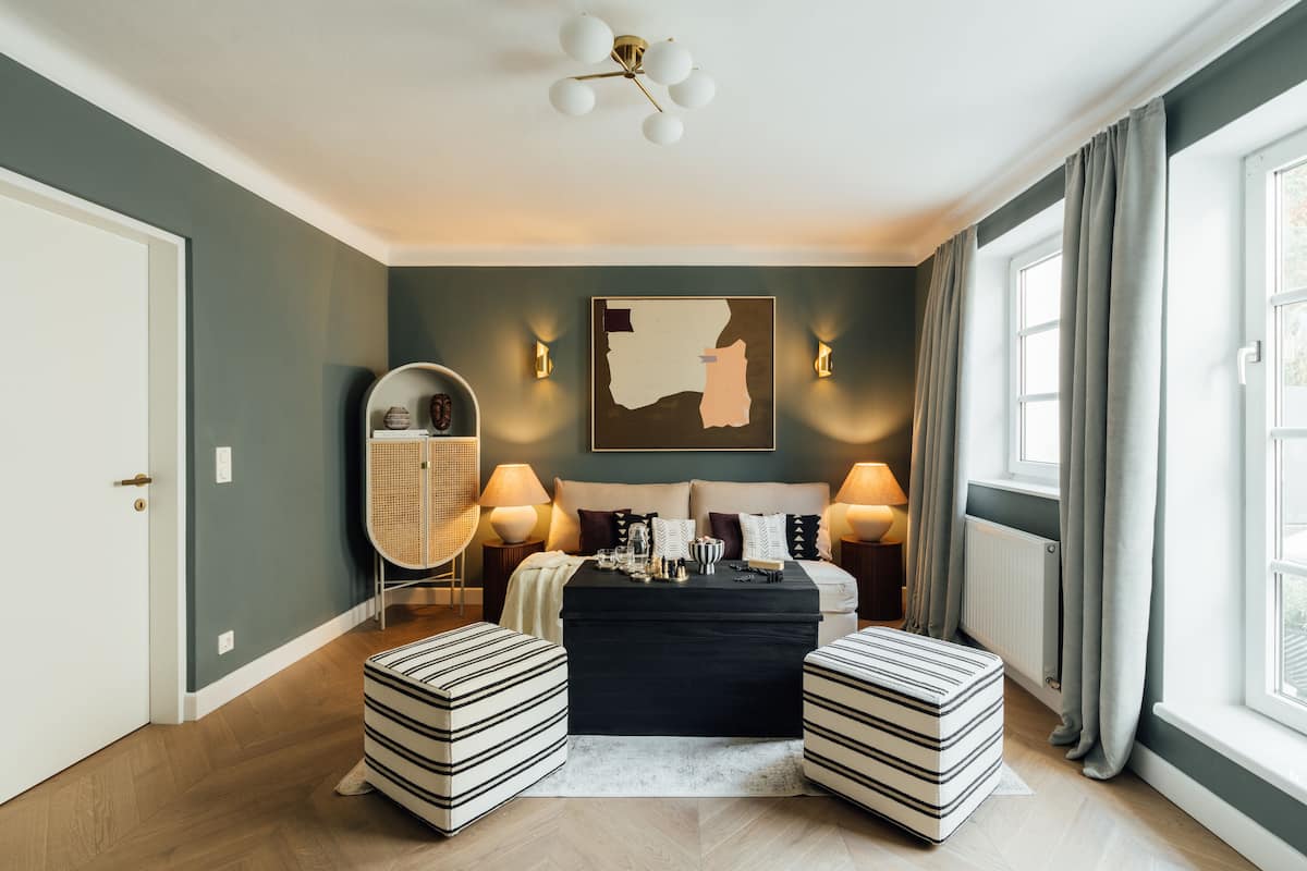Een moderne slaapkamer met een bed, twee poefjes, een bijzettafeltje, een lamp en een spiegel aan de muur.
