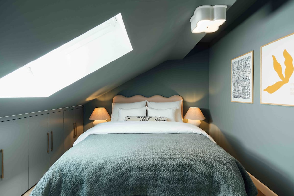 Een slaapkamer met een dakraam, een bed met witte beddengoed, twee bedlampjes en kunst aan de muur.