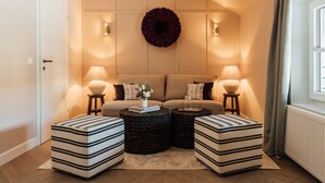 A cozy living room with a sofa, two ottomans, a round coffee table, and two lamps.