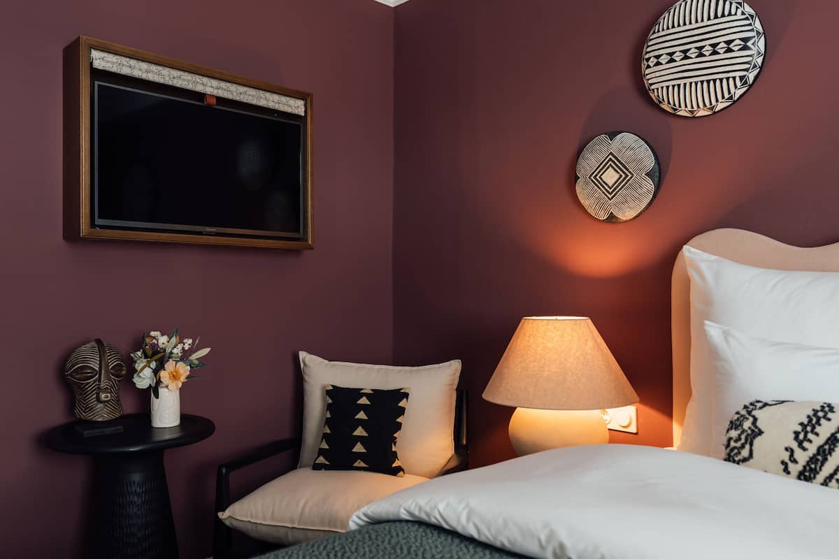 Een hotelkamer met een bed, nachtkastje, lamp, een wandtelevisie en decoratieve wandkunst.