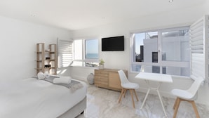 A modern bedroom with a bed, a desk, a chair, a TV, and large windows. - Endless Summer Beach House (Cape Town)