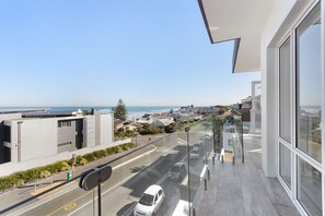 A balcony with a clear view of a road and ocean, modern architecture, and a glass railing. - Endless Summer Beach House (Cape Town)
