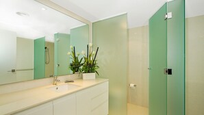 A modern bathroom with a large mirror, a sink, a shower, and a toilet.