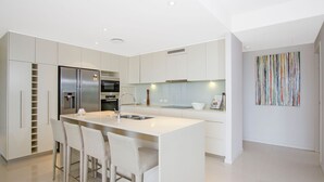 A modern kitchen with a central island, bar stools, stainless steel appliances, and a minimalist design.