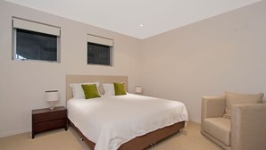 A modern hotel room with a large bed, two bedside tables, a chair, and two windows.