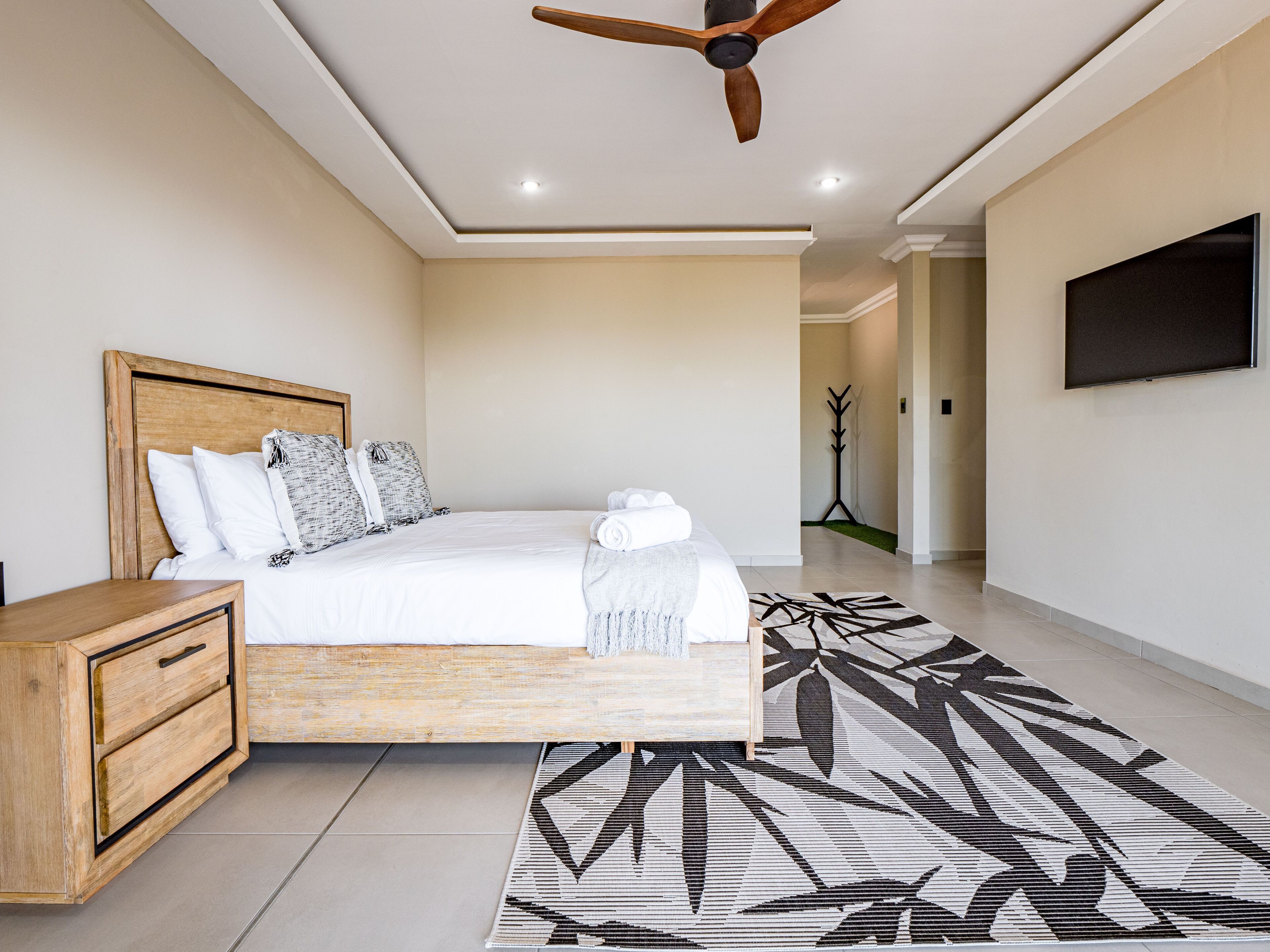 Une chambre à coucher moderne avec un cadre de lit en bois, une table de chevet, un grand tapis et un ventilateur de plafond.