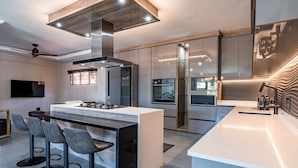 A modern kitchen with a central island, bar stools, built-in appliances, and a large window. - One on Chelsea (Umhlanga)