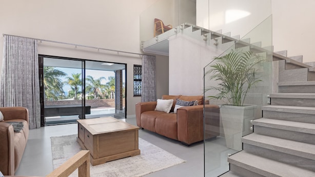 A modern living room with a sofa, coffee table, and a staircase with glass railings. - One on Chelsea (Umhlanga)