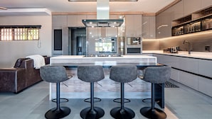 A modern kitchen with a central island, bar stools, and a built-in oven. - One on Chelsea (Umhlanga)