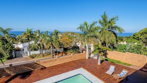 A swimming pool with a wooden deck, palm trees, and a view of the ocean. - One on Chelsea (Umhlanga)