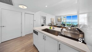 A modern kitchen with a large sink, white cabinets, and a view of the ocean through large windows. - 1-BD Condo in Coconut Grove | Water Views (Miami)