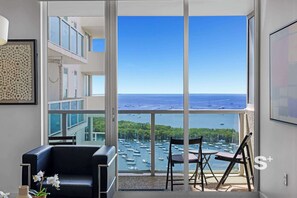Ein geräumiger Balkon mit freiem Blick auf das Meer und Boote, eine schwarze Ledersofa und ein kleiner Tisch mit Stühlen.