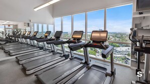 A gym with treadmills aligned against a wall with large windows offering a city view. - 1-BD Condo in Coconut Grove | Water Views (Miami)