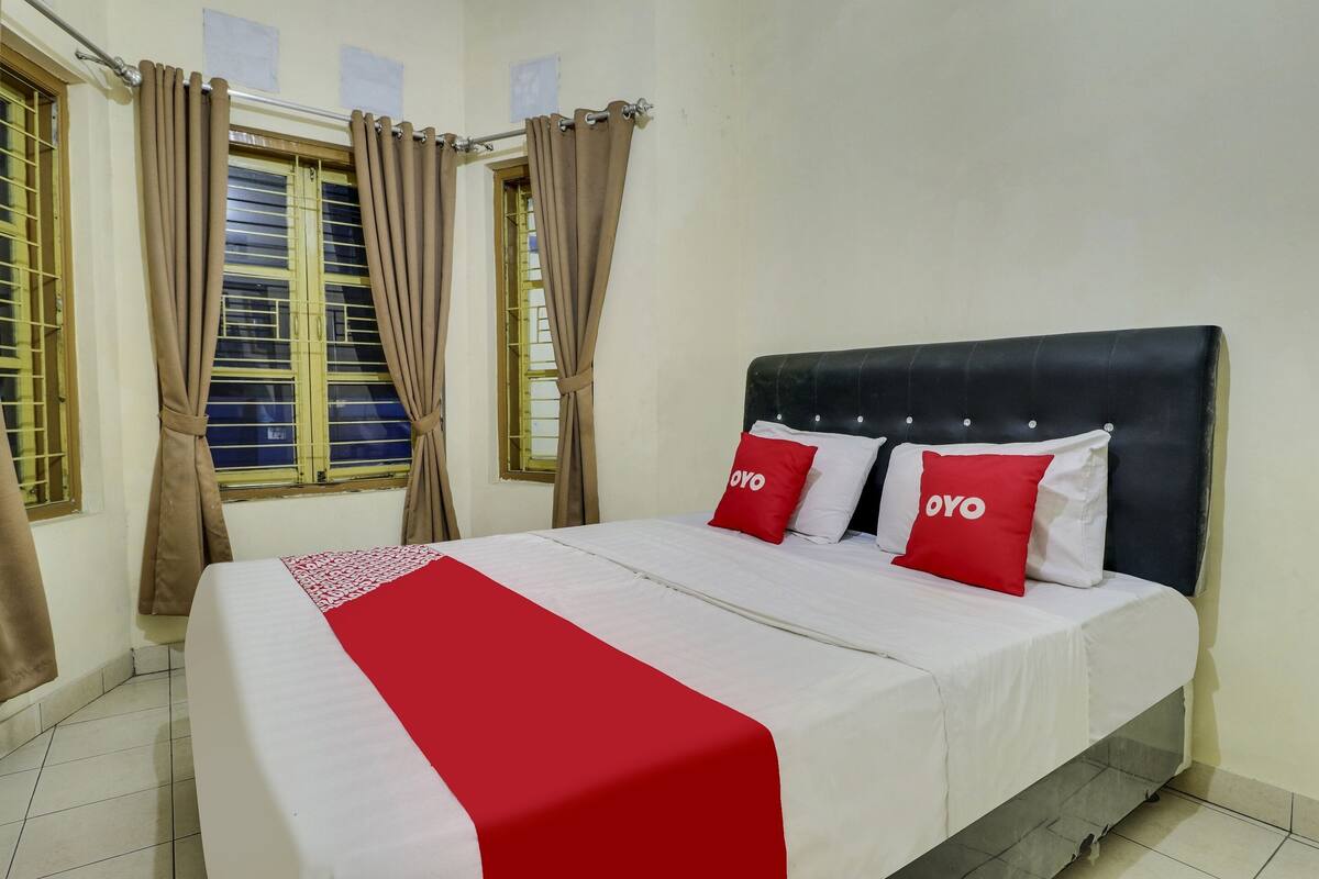 A neatly made bed with a red and white bedspread and two red pillows with the word "OYO" on them.