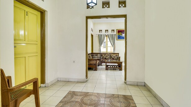 A hallway with a yellow door, a wooden bench, and a patterned rug. - Hotel O My Guest House Syariah (Padalarang)