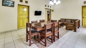 A dining area with a wooden table and chairs, a television, and a patterned rug. - Hotel O My Guest House Syariah (Padalarang)