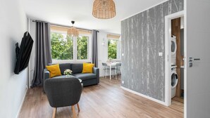 Una sala moderna con un sofá gris, una mesa de comedor y una lavadora al fondo.