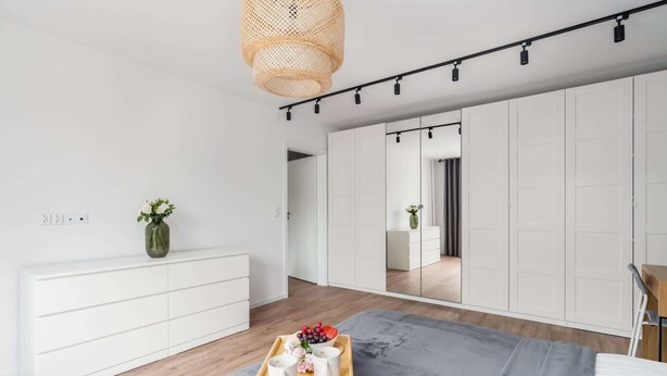 Un dormitorio moderno con un aparador de madera, una colcha gris y una bandeja con tazas y flores.