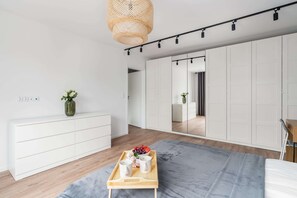 A modern bedroom with a wooden dresser, a gray bedspread, and a tray with cups and flowers. - Stylish Apartment with Balcony | Workspace (Poznan)