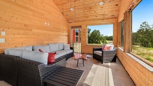 L’intérieur d’un chalet en bois, avec un canapé, deux fauteuils, une petite table et une vue sur l’extérieur.