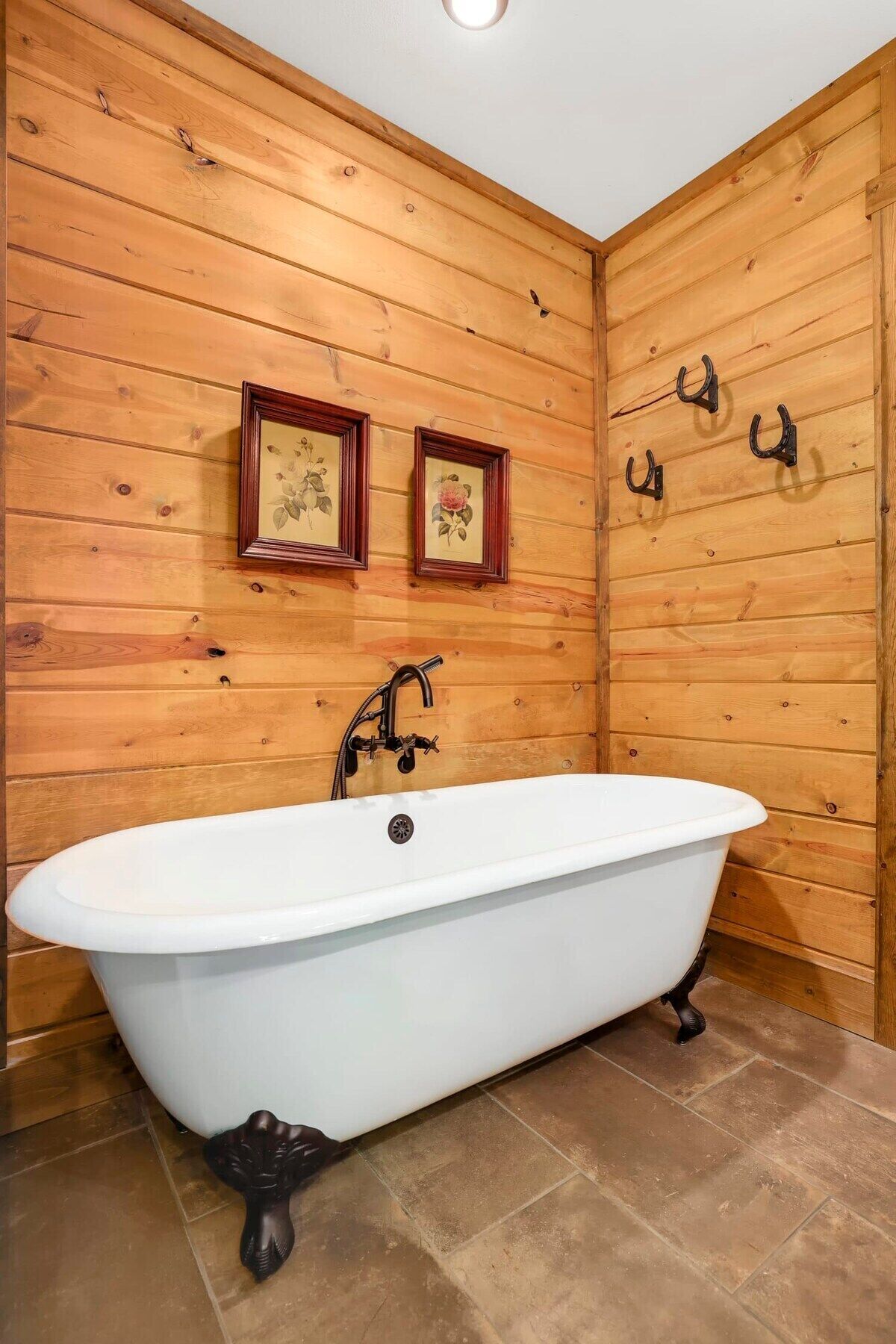 A bathroom with a freestanding bathtub, wooden wall paneling, a framed floral picture, and a towel rack.