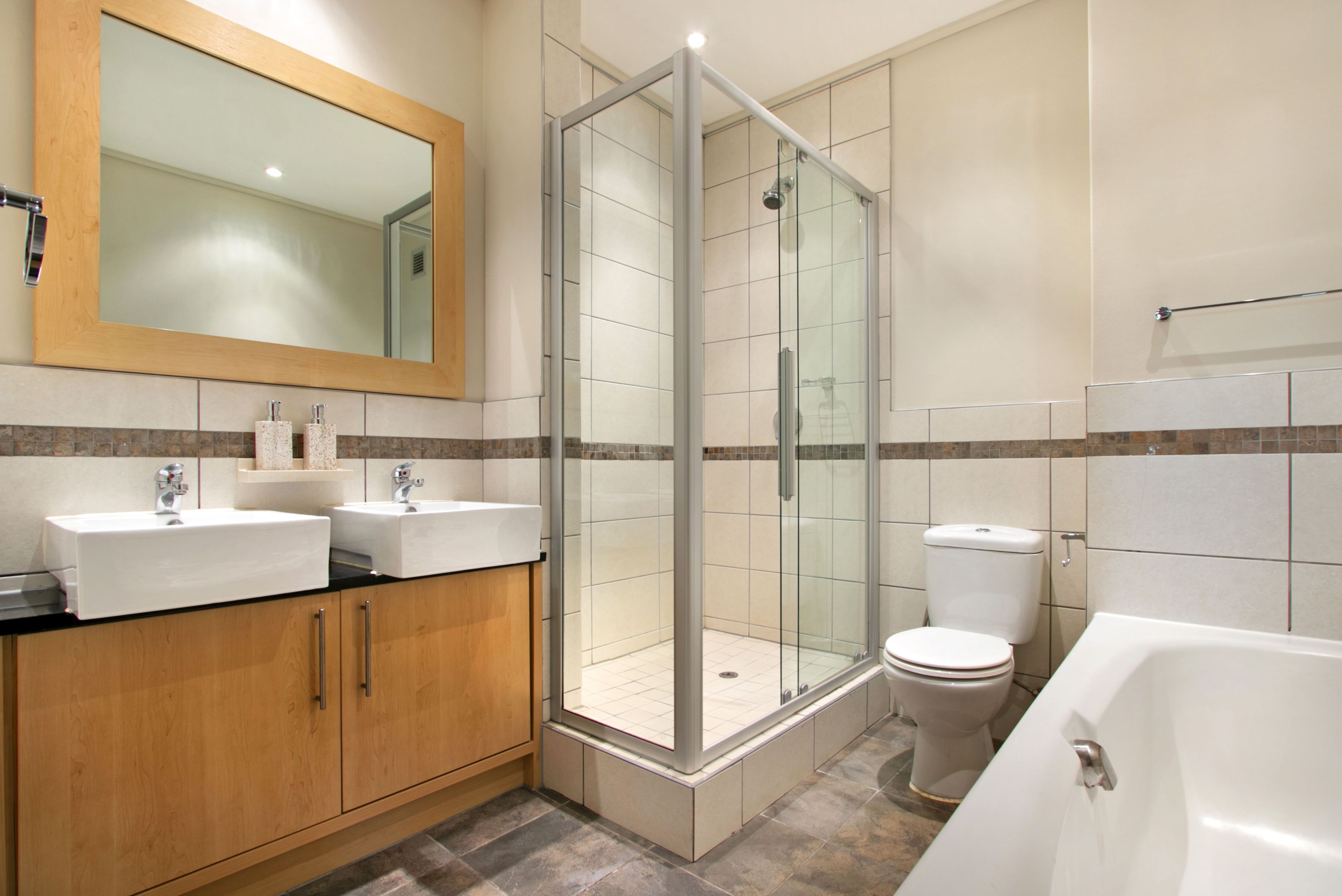 A modern bathroom with a glass-enclosed shower, two sinks, a toilet, and a bathtub.