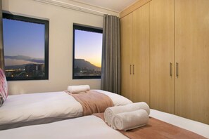 A hotel room with two beds, a large wardrobe, and a city view through the windows.
