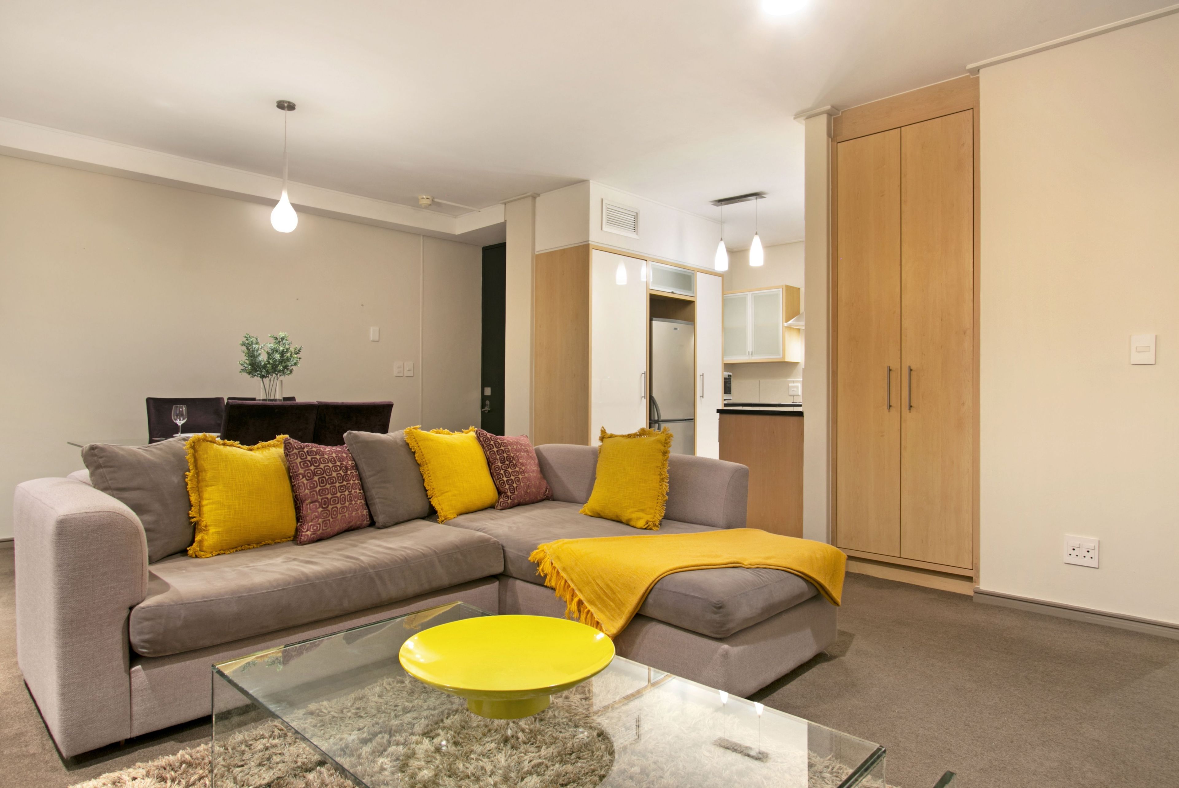 A modern living room with a grey sectional sofa, yellow throw pillows, and a glass coffee table.