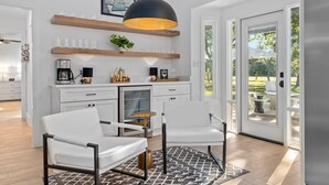 A modern kitchen with white cabinetry, a coffee machine, and a pendant light. There are two white chairs and a small round table. - Three Dog Ranch - Pool, Game Room & Sleeps 18 (Driftwood)