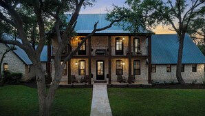 A two-story stone house with a covered porch, a stone pathway leading to the entrance, and a metal roof. - Three Dog Ranch - Pool, Game Room & Sleeps 18 (Driftwood)