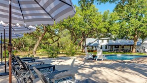 A pool area with lounge chairs, a swimming pool, and a house in the background. - Three Dog Ranch - Pool, Game Room & Sleeps 18 (Driftwood)