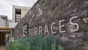 Un muro de piedra con el texto "THE TERRACES" y un edificio moderno al fondo.